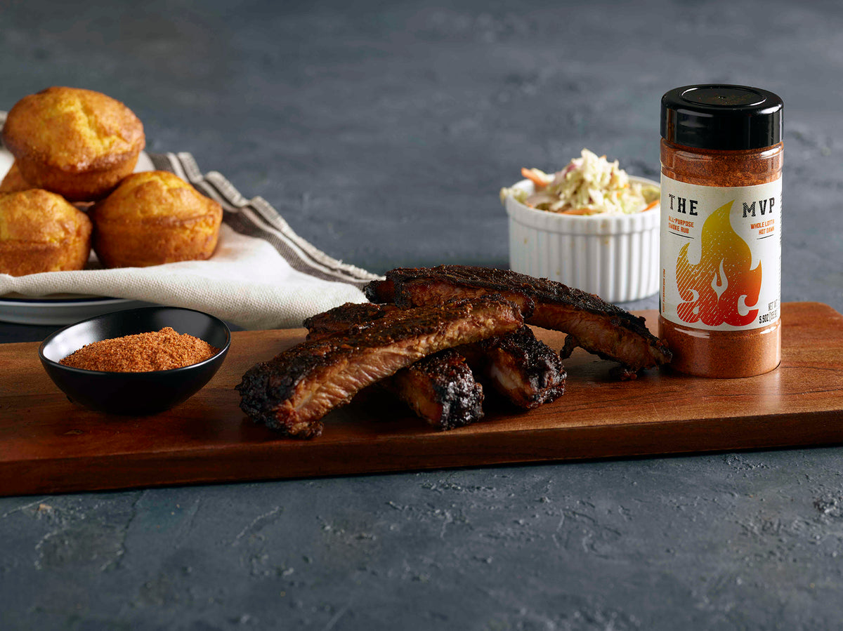 The MVP All-purpose rub on a cutting board with cooked rubs and sides